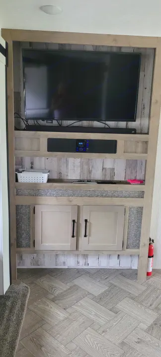 RV rental living space: integrated entertainment center with TV, media unit, shelving, and cabinets. Features wood-look details.. Palomino RBFQ 2022