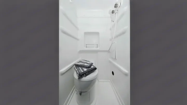 Functional RV rental wet bath. Features a compact toilet with folded towels, a shower, and an integrated shelf.. Winnebago Solis 2021