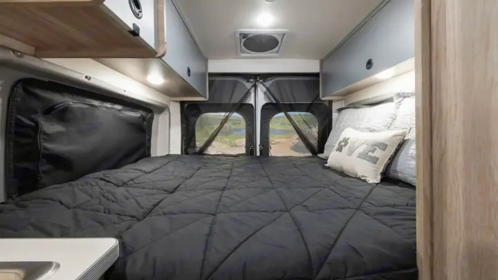 Inside an RV rental: a comfortable bed, scenic rear view, and overhead storage in this camper van.. Winnebago Solis 2021