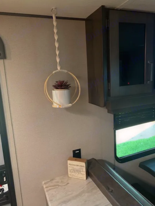 Cozy RV rental interior features: wall-mounted TV, window, and a charming hanging plant with rope hanger.. Grand Design Transcend Xplor 2022