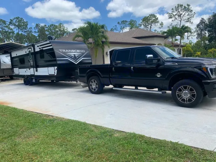 Black pickup truck towing a black/white Transcend travel trailer, ready for an RV rental journey on a sunny day.. Grand Design Transcend Xplor 2022