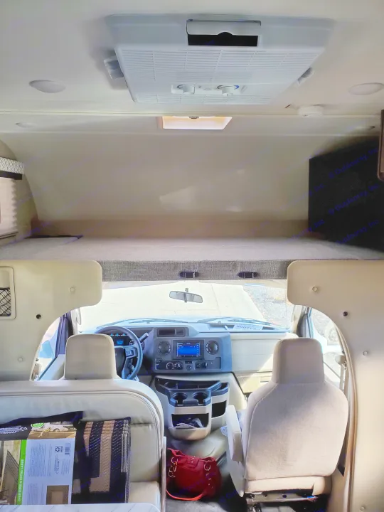 View inside an **rv rental**, from the living area to the front cab and overhead sleeping bunk. Includes AC and dashboard.. Thor Coleman 2023