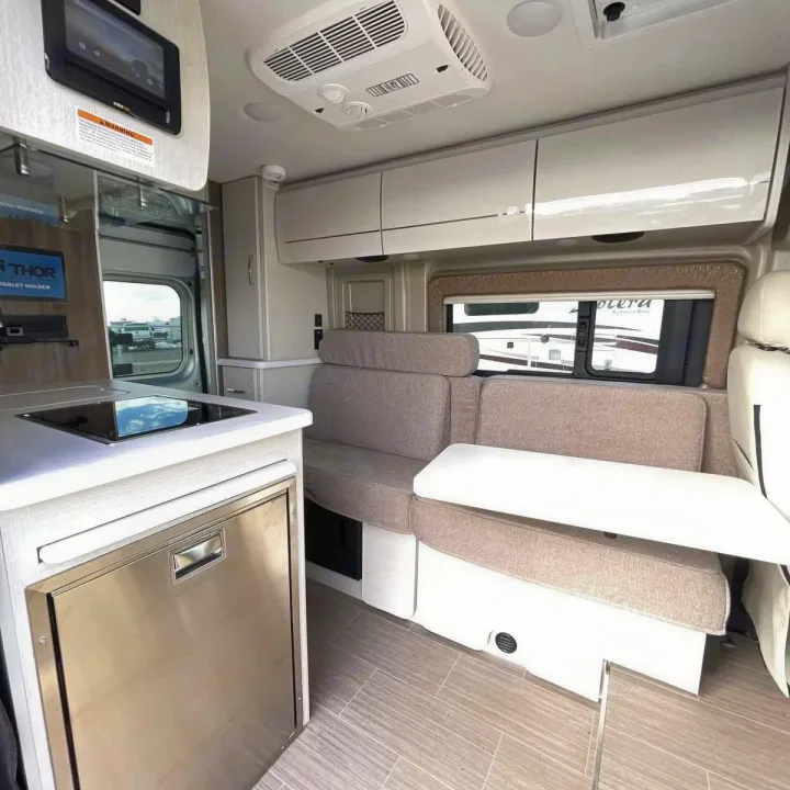 Bright rv rental interior featuring a compact kitchen with stove, refrigerator, and a comfortable dinette with storage.. Thor Rize 2022
