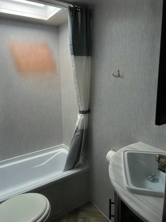 Compact RV rental bathroom: sink, toilet, and shower with striped curtain. Practical for travel.. Forest River Wildwood X-Lite 2023