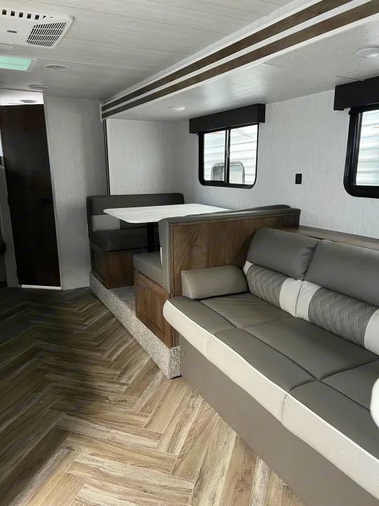 RV rental's modern living space with gray seating, striking herringbone flooring, light walls, and ample windows for comfort.. Forest River Wildwood X-Lite 2023