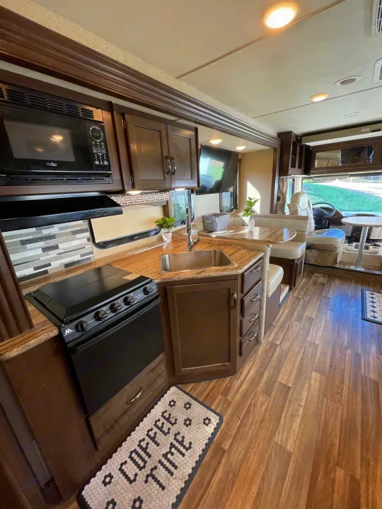 Spacious and modern RV rental interior featuring a full kitchen with microwave, stovetop, and sink, plus a comfy dinette area.. Thor A.C.E. 2017