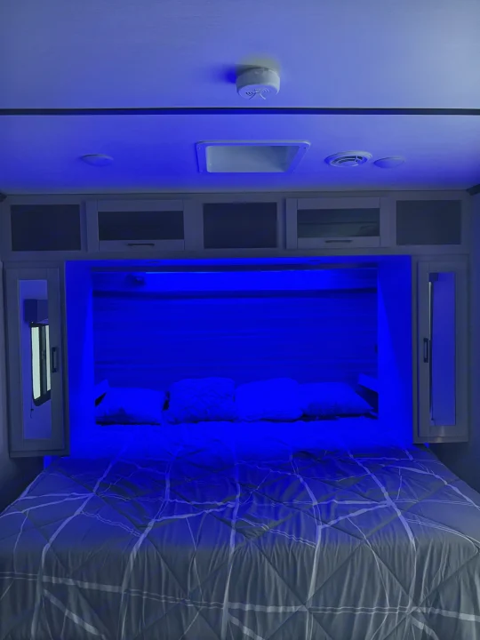 Cozy RV rental bedroom with modern blue accent lighting, a comfortable bed, and overhead storage.. Crossroads RV Cruiser Aire 2022