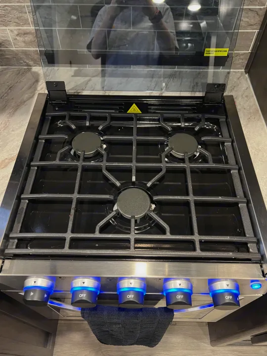 RV rental kitchen: Three-burner gas stove with a protective glass cover and illuminated controls. Safety warnings visible.. Crossroads RV Cruiser Aire 2022