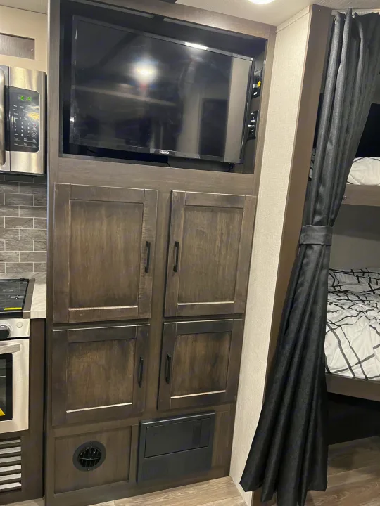 Cozy RV rental interior: kitchen with microwave, TV, ample storage, and bunk beds with a privacy curtain.. Crossroads RV Cruiser Aire 2022