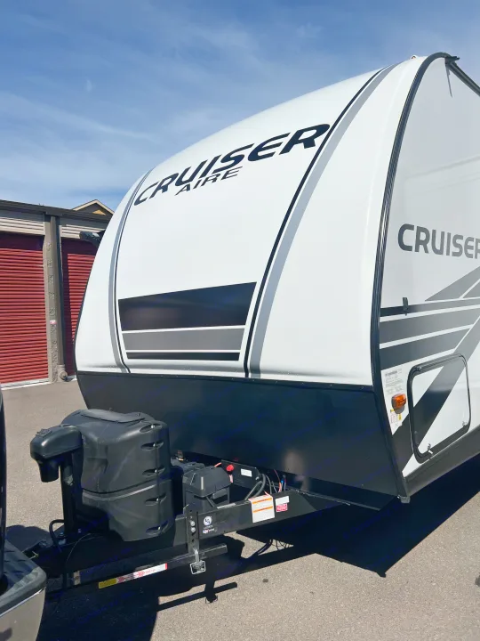 This white Cruiser Aire travel trailer, ideal for RV rental, features its front profile, hitch with propane tanks, and side graphics.. Crossroads RV Cruiser Aire 2022