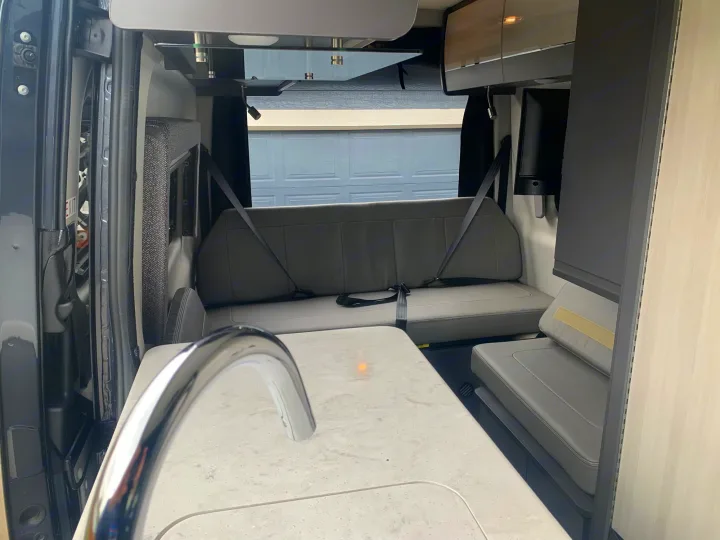 Inside a modern **rv rental**: A well-equipped kitchen area with a sink and a cozy rear seating/dining space with seatbelts.. Mercedes-Benz Sprinter 2022