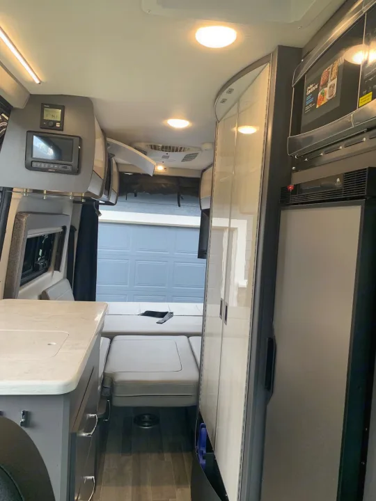 Inside a modern RV rental, featuring a kitchen area, adaptable bed/seating, microwave, and refrigerator.. Mercedes-Benz Sprinter 2022