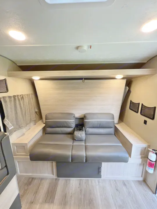 RV rental living area: modern gray sofa with cupholders, fold-down bunk, overhead storage, and wood-look flooring.. Coachman Catalina Catalina Summit Series 7 184BHS 2022