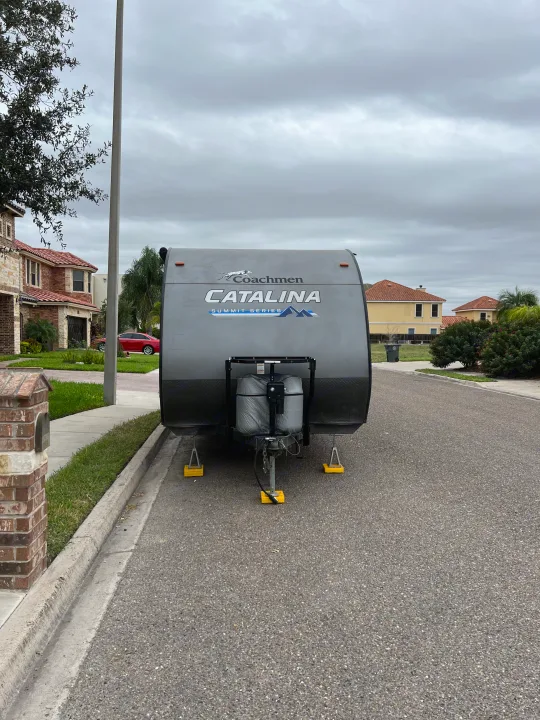 Front view of a grey Coachmen Catalina travel trailer, stabilized on yellow blocks, parked on a suburban street. Perfect for an RV rental.. Coachman Catalina Catalina Summit Series 7 184BHS 2022