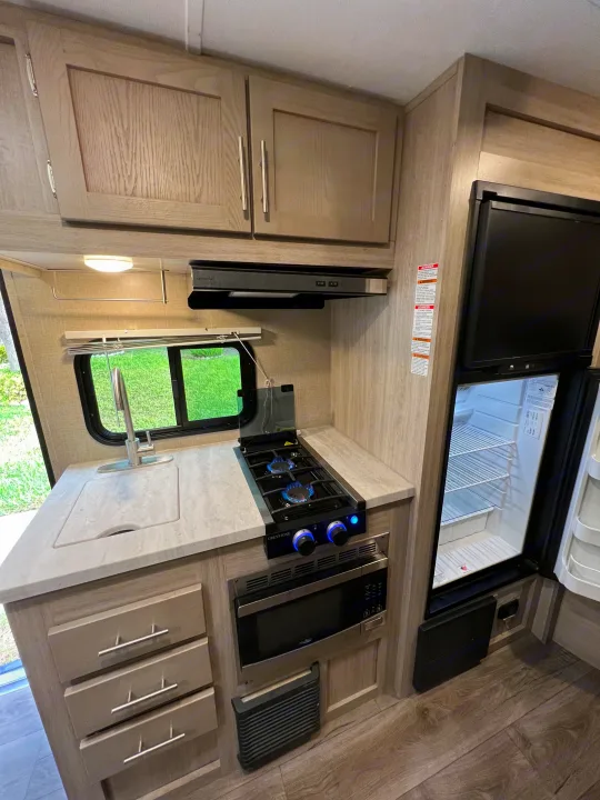 Explore this RV rental's compact kitchen with sink, two-burner stove, microwave, and open fridge.. Coachman Catalina Catalina Summit Series 7 184BHS 2022