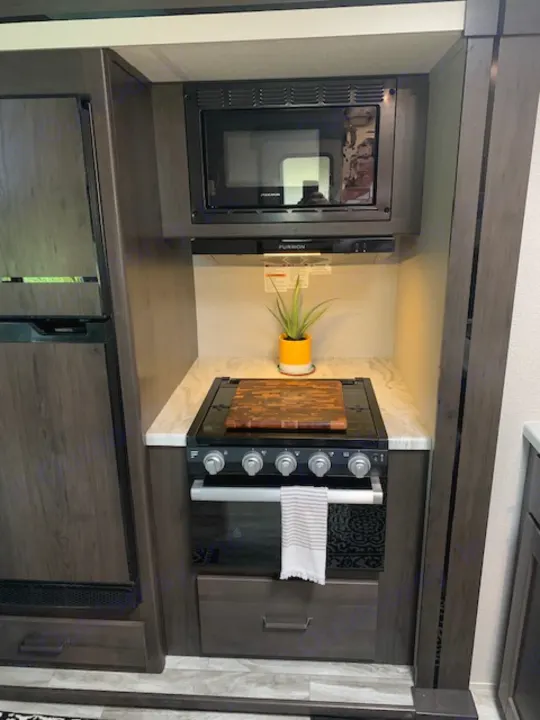 Explore the functional kitchen of this RV rental, with built-in microwave, compact oven, and under-counter fridge.. Grand Design Transcend Xplor 2022
