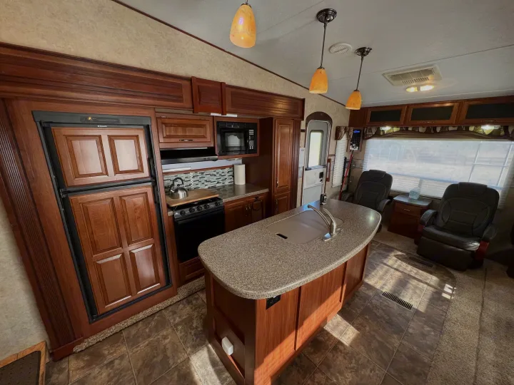 Spacious RV rental interior with full kitchen, island, and comfortable recliners. Warm wood tones throughout.. Keystone Cougar 2013