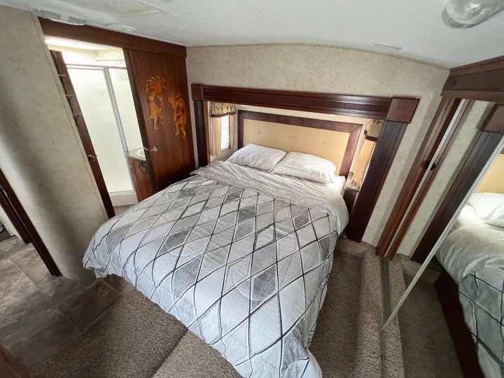 RV rental bedroom: a cozy space with a patterned bed, wood headboard, carved door to shower, and mirrored closet.. Keystone Cougar 2013