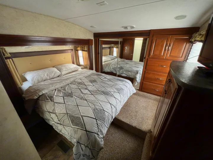 This RV rental bedroom features a queen bed, mirrored closet, wood dresser, and carpeted steps. Cozy interior.. Keystone Cougar 2013