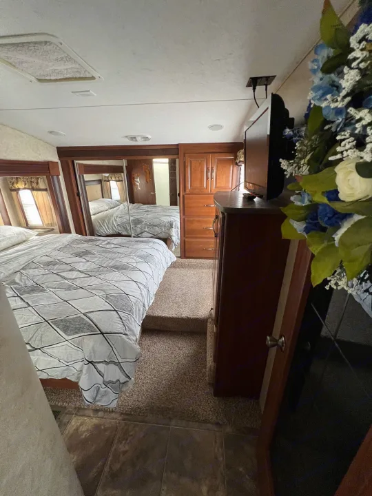 Experience comfort in this RV rental bedroom. Features a large bed, mirrored closet, TV, and carpeted steps to living area.. Keystone Cougar 2013
