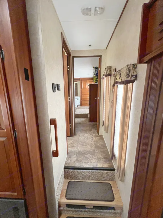 RV rental interior: A hallway with steps leading to a bedroom, featuring wood cabinets and window blinds, for a comfortable travel experience.. Keystone Cougar 2013