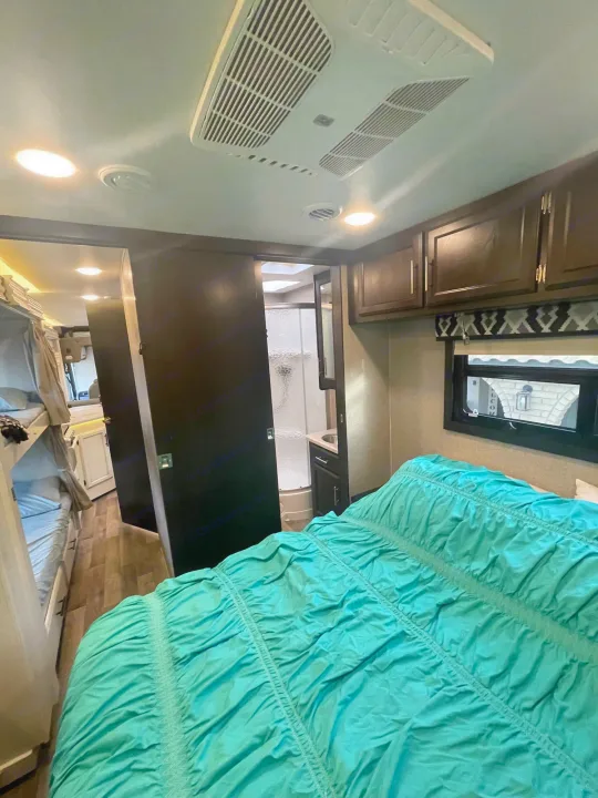 RV rental bedroom with teal comforter, visible bunk beds, and en-suite bathroom. Enjoy mobile comfort on your next trip!. Entegra Coach Vision 29f Bunk house model 2021