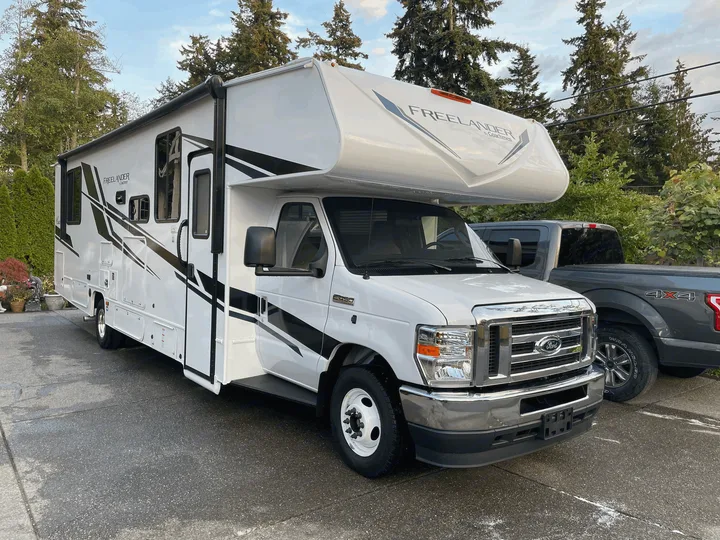 White Coachmen Freeland Class C RV rental, featuring sleek graphics and parked in a driveway on a clear day.. Forest River Coachmen Freelander Premier 2022