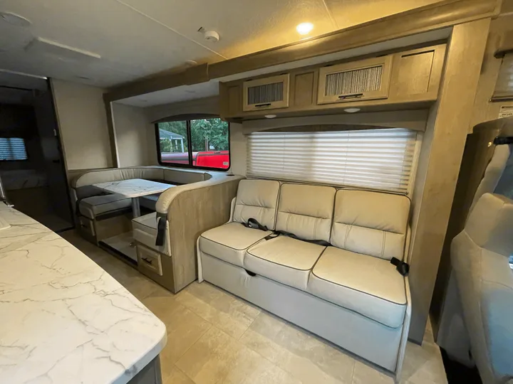 Comfortable rv rental living space: dinette, sofa with seatbelts, overhead cabinets, and bright interior.. Forest River Coachmen Freelander Premier 2022
