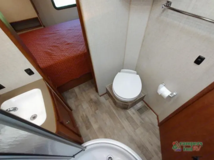 This RV rental features a compact bathroom with a toilet, sink, and shower, leading to a cozy bedroom area with a bed.. Winnebago Vista 2017