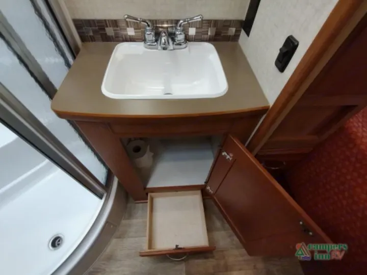 Compact RV rental bathroom: vanity, sink, pull-out storage drawer, and shower. TP roll visible under sink.. Winnebago Vista 2017