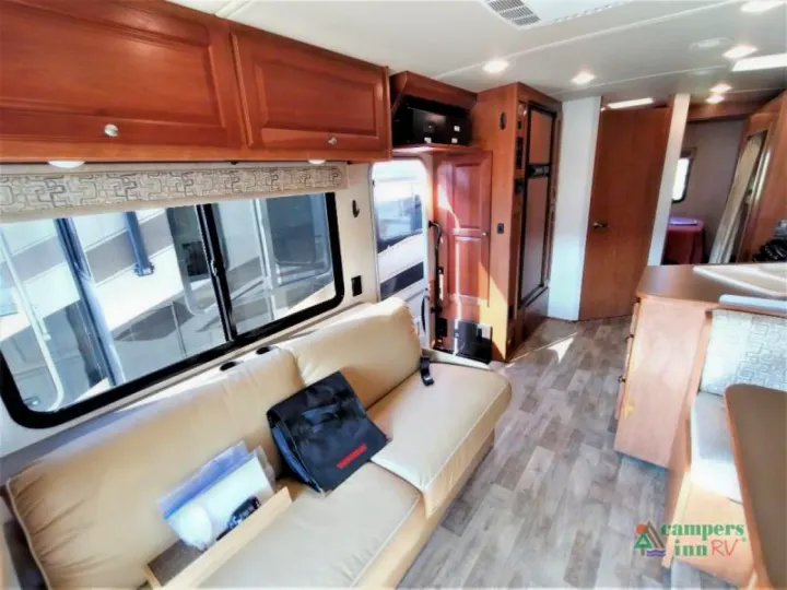 Inside an RV rental: a bright living area with a tan sofa, wood cabinets, refrigerator, & rear access to a bed/bath area.. Winnebago Vista 2017