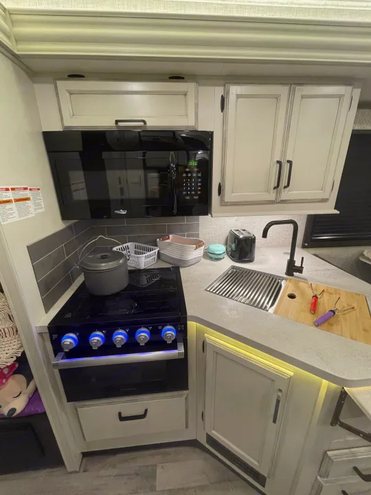This compact, well-equipped RV rental kitchen features a microwave, stove, sink, and under-cabinet lighting.. Entegra Coach Odyssey 2023