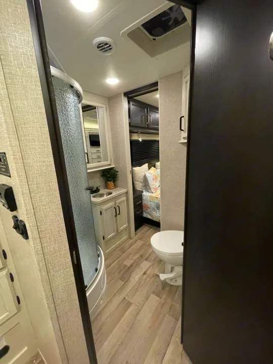 RV rental interior: A narrow view of a compact bathroom with shower, sink, and toilet, leading to the bedroom.. Entegra Coach Odyssey 2023