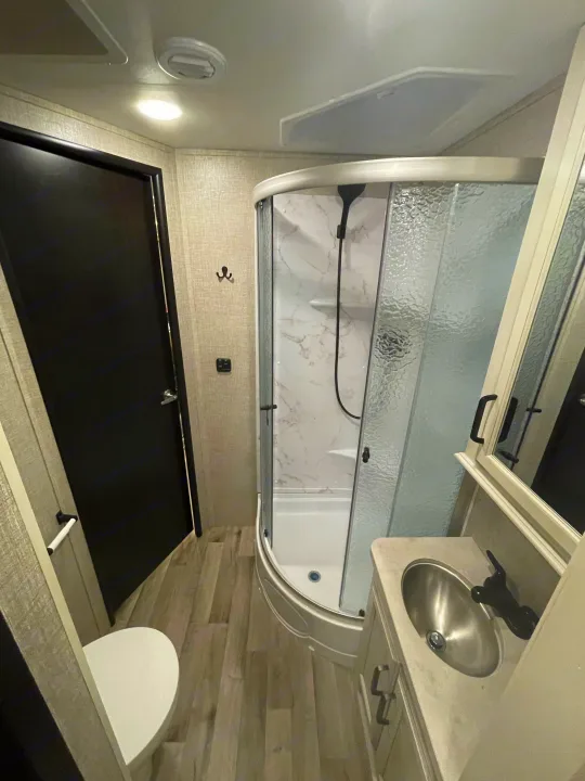 Inside a spacious RV rental bathroom: featuring a curved shower, vanity with sink, and toilet for comfortable travel.. Entegra Coach Odyssey 2023