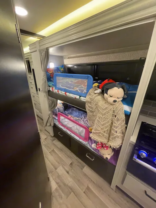 Cozy RV rental interior: bunk beds with safety rails, stuffed toys, and light wood flooring. Perfect for family trips.. Entegra Coach Odyssey 2023