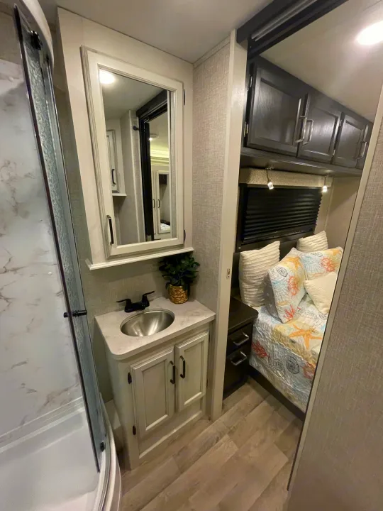 RV rental interior showcasing a modern bathroom with shower and vanity, alongside a cozy bedroom.. Entegra Coach Odyssey 2023