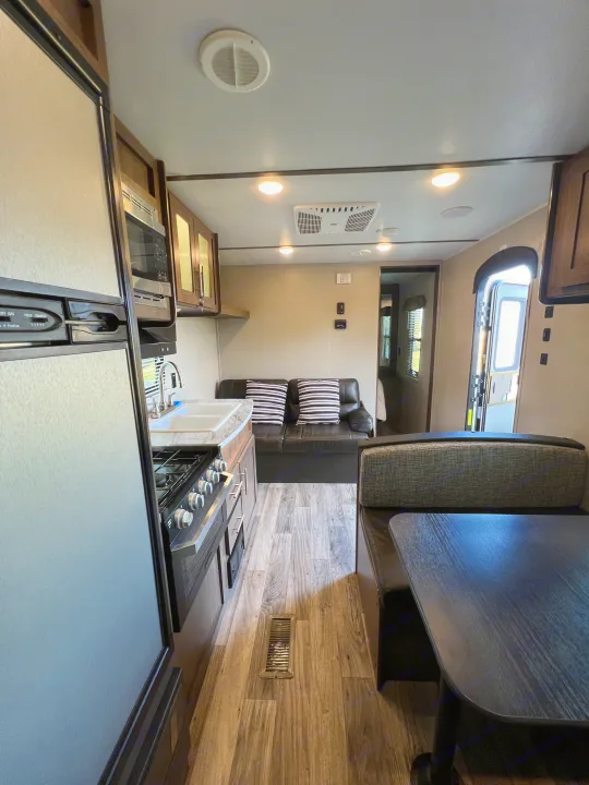 RV rental interior showing a kitchen with fridge, stove, and sink, alongside a living area with a sofa and dinette.. Keystone RV Hideout LHS 2020