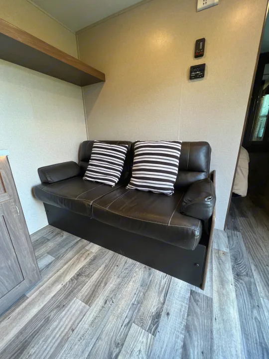 Cozy RV rental interior showing a black couch with striped pillows and grey wood-look flooring.. Keystone RV Hideout LHS 2020
