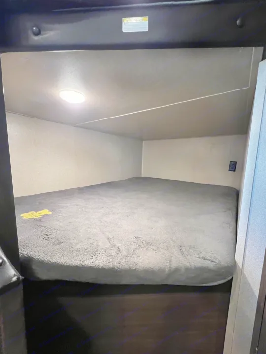 Compact bunk bed sleeping area in an RV rental, featuring a cozy gray mattress, overhead light, and power outlet for a comfortable stay.. Keystone RV Hideout LHS 2020