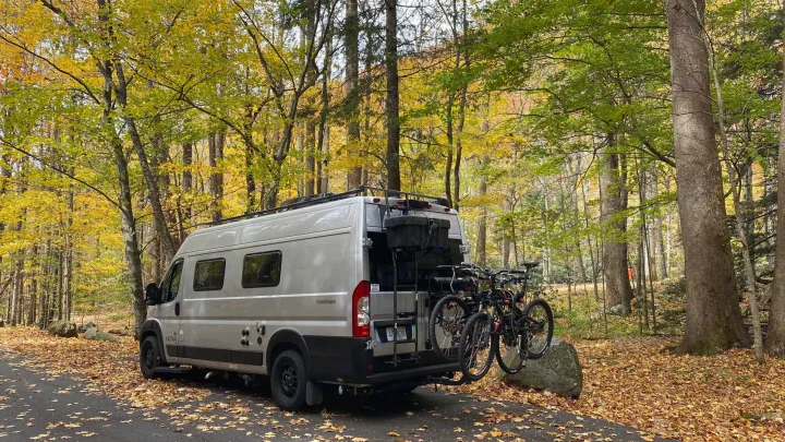 Fall RV rental adventure: A camper van with bikes parked on a leaf-covered road, surrounded by autumn trees.. Coachmen Nova20 Li3.  Lithium / generator free silent power 2022