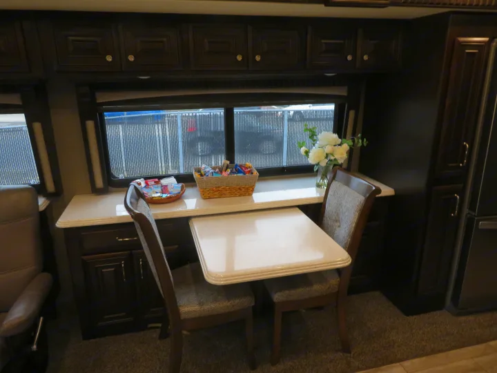 Inviting RV rental interior: dining table, chairs, counter with snacks & flowers, and full kitchen amenities.. Monaco Signature 2019