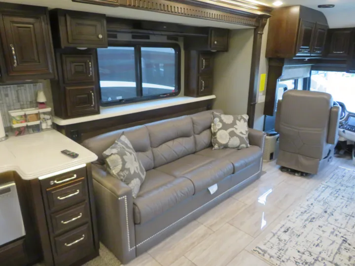 This RV rental interior features a modern living space with a grey sofa, kitchen area, and ample cabinetry for comfortable travel.. Monaco Signature 2019