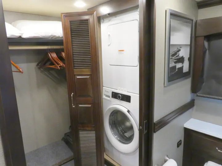 This compact RV rental features a stacked washer/dryer unit, a closet with hangers, and an upper bunk with pillows.. Monaco Signature 2019