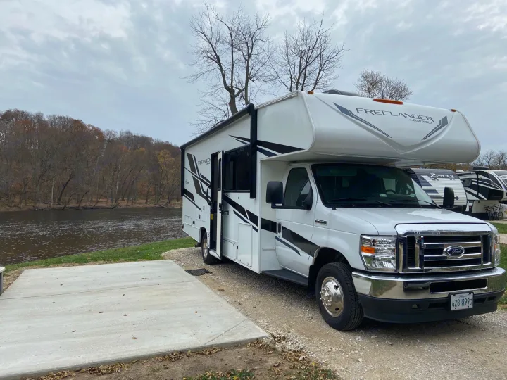 Experience nature with this RV rental. Parked riverside at a quiet campsite under a cloudy sky, ready for your next travel adventure.. Forest River Coachmen Freelander Premier 2022