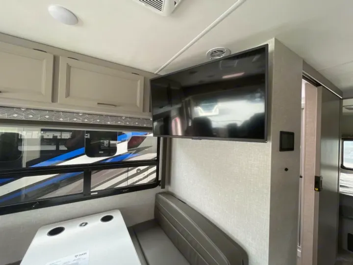 Experience comfort in this RV rental interior, featuring a cozy dinette, overhead cabinets, and a wall-mounted TV for your journey.. Ford Windsport 2023