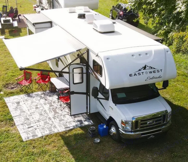 An East West Entrada RV rental parked on grass, ready for camping with an extended awning, chairs, mat, and pet bowls.. East to West Entrada 2600DS 2022