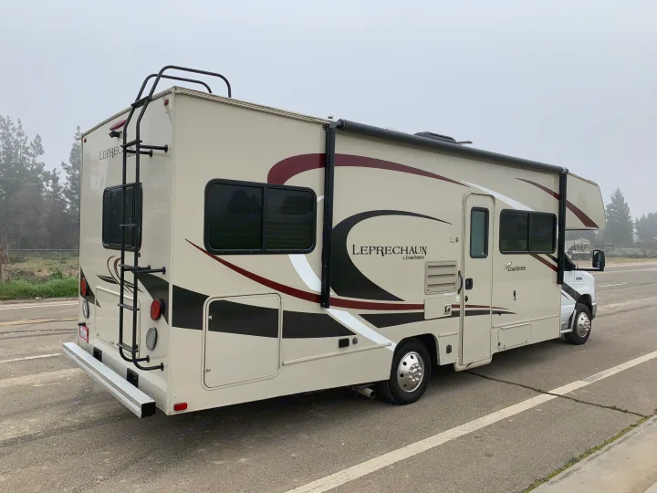 Side view of a light-colored Coachmen Leprechaun motorhome, perfect for an rv rental adventure on an overcast day.. Forest River Coachmen Leprechaun 2020