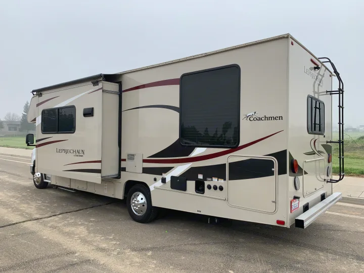 This Coachmen Leprechaun RV rental in beige and maroon shows its extended side and rear ladder, parked on pavement.. Forest River Coachmen Leprechaun 2020