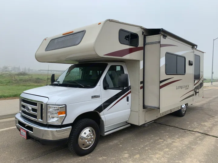 White and beige Class C RV rental (Coachmen Leprechaun) parked on asphalt, ready for adventure on a misty day. Visit roadbearrv.com.. Forest River Coachmen Leprechaun 2020