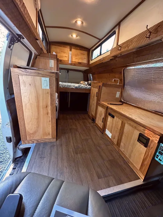 Inside a unique RV rental: custom wood interior, bed, kitchen counter, and wood-look flooring for cozy travel.. Chevrolet Express EXT 3500 2008